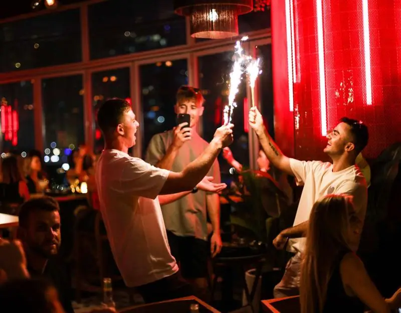 Guests raising sparkler bottles under the neon wall