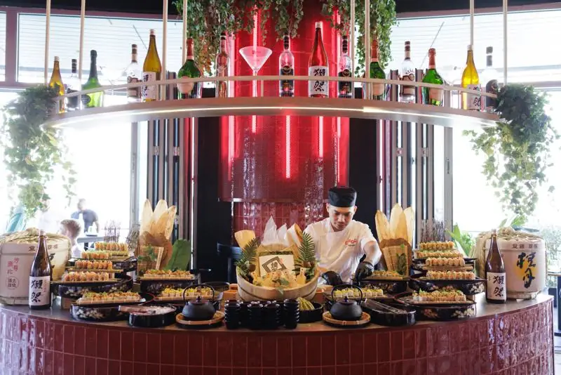 The live sushi station at Saturday brunch, the chef plating rolls under the neon